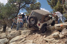 Rock crawlers lend physical and mental support to help a jeep make it over the hump.