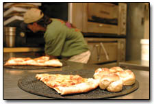 A slice of pizza and a handful of rolls wait to be consumed as bill Bercheni works in the Homeslice kitchen.