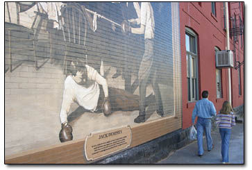 A pair of holiday shoppers pass the Jack Dempsey mural outside El Rancho.