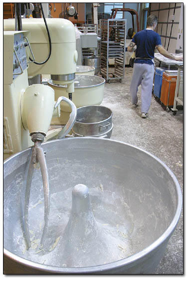 Peter Demain rolls dough behind a row of large mixers at Jean-Pierre Bakery.