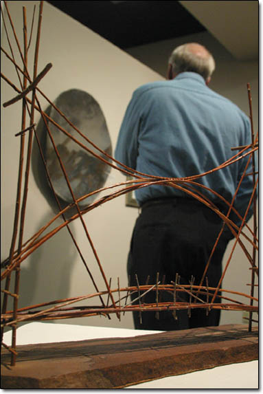 "The Good Luck Bridge #4," made of willow, wire, and stone by Carolynn L. Wood sits under a display light as Steve Redding peruses in the background.