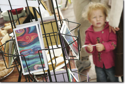 One-year-old Eden O'Donnell takes in the Farmers Market excitement from beneath a rack of greeting cards.