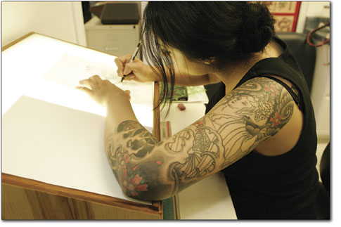 Tatti Vladis, of Blue Tiger Tattoo, works on a sketch from atop
her light table as she displays her own art on her left arm.