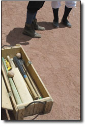 An old box filled with historic bats and balls sits open on the
field as two players stand nearby. Baseballs of the 19th century
were typically much softer, making playing bare-handed much less
painful.