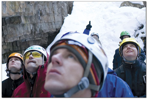 Students of the ice climbing clinic look upward as an insturctor
demonstrates the proper technique for climbing a frozen
waterfall.
