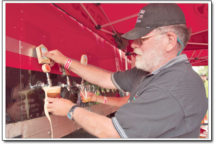 Volunteer Dennis Pierce takes a break from reading
theTelegraphto make sure all the brews are filled to the brim in
the New Belgium tent Saturday afternoon.
