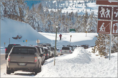 A line of cars sits along the side of the road near the entrance
to Andrews Lake as a cross-country skier makes his way along the
path.