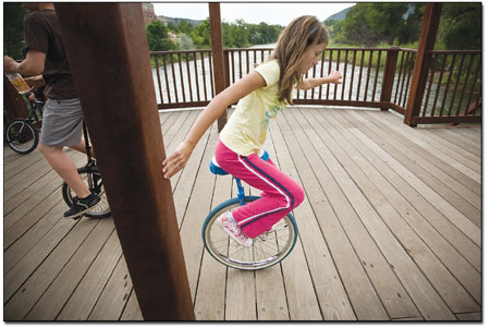 Claire Fenton pushes off from a support beam while getting the
feel of a unicycle on the bridge at Cundiff Park.
