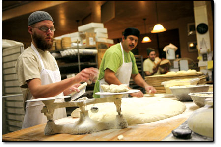 Mike Burr (left) carefully weighs fresh dough then executes a
sporty dough toss to Gilberto Uribe (right), who preps the dough
for baking.