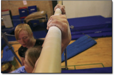 A coach helps spot a young gymnast learning the how to dismount
from the bars.